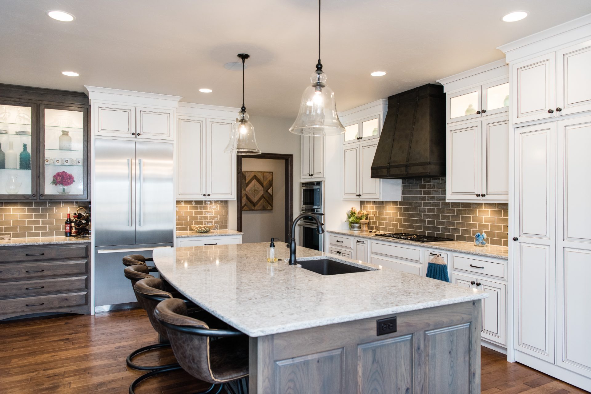 New Quay Cambria Quartz Kitchen Countertops with White and Gray Wood Cabinets, Wood Floors, and Bar Stools