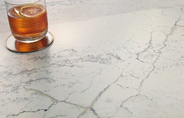 Close-up view of Cambria Windsor Steel Satin Ridge Quartz, showcasing its steel-toned wave patterns, warm honey-colored sand backdrop, and contrasting cool charcoal elements installed for kitchen countertops.